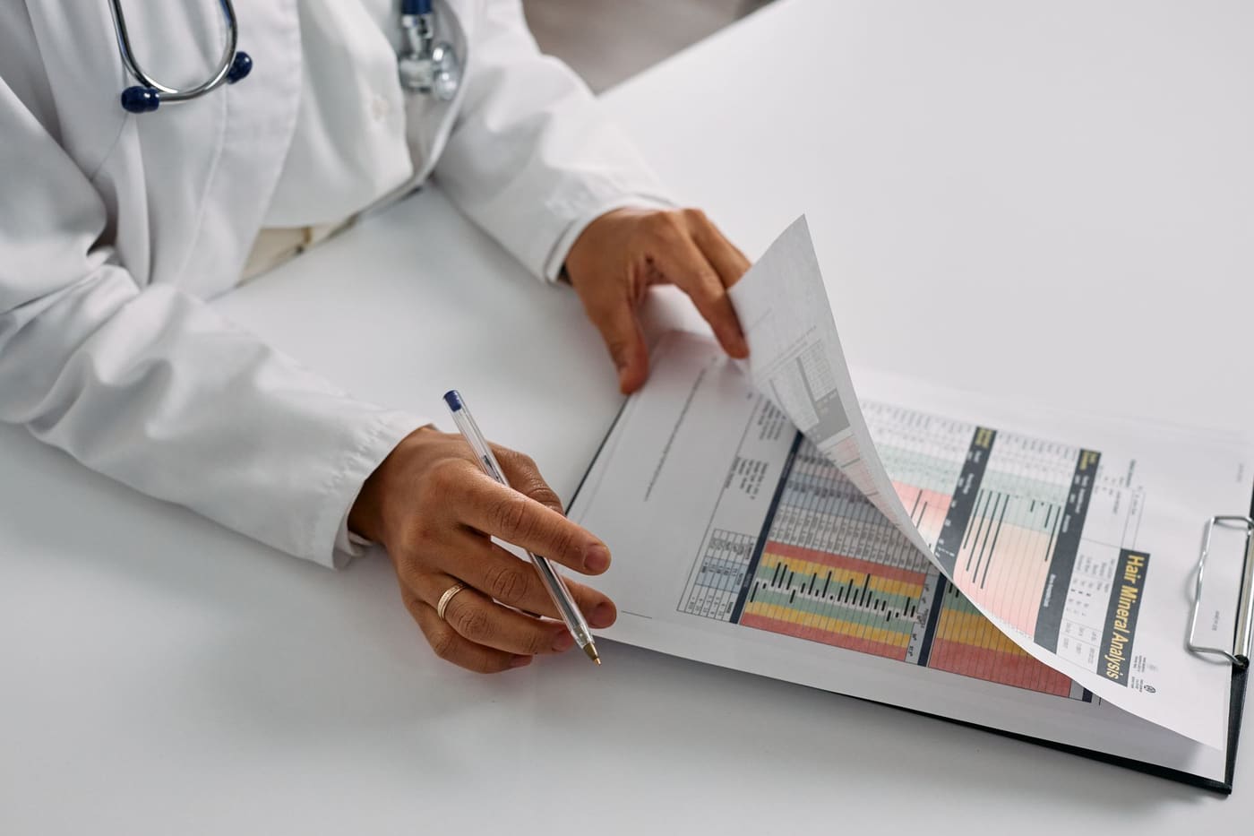 A doctor in a white coat reviewing printed reports on a clipboard at a desk
